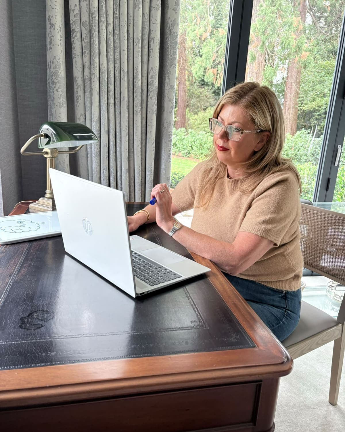 Jo Smith working at her desk beside a green desk lamp, with the garden behind her