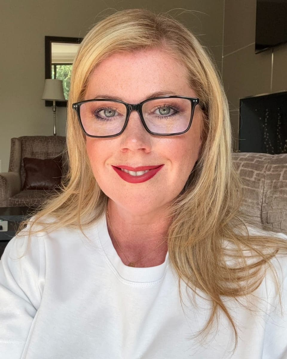 Jo Smith smiling at the camera, blonde hair, black-framed glasses and a white top