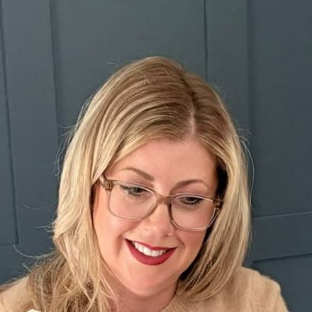 Jo Smith smiling and looking down, in front of a dark blue panelled wall